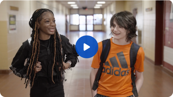 This is the placeholder image for the Tale of Two Cities video. Two middle school-aged children walk down an Alabama school hallway smiling and talking.